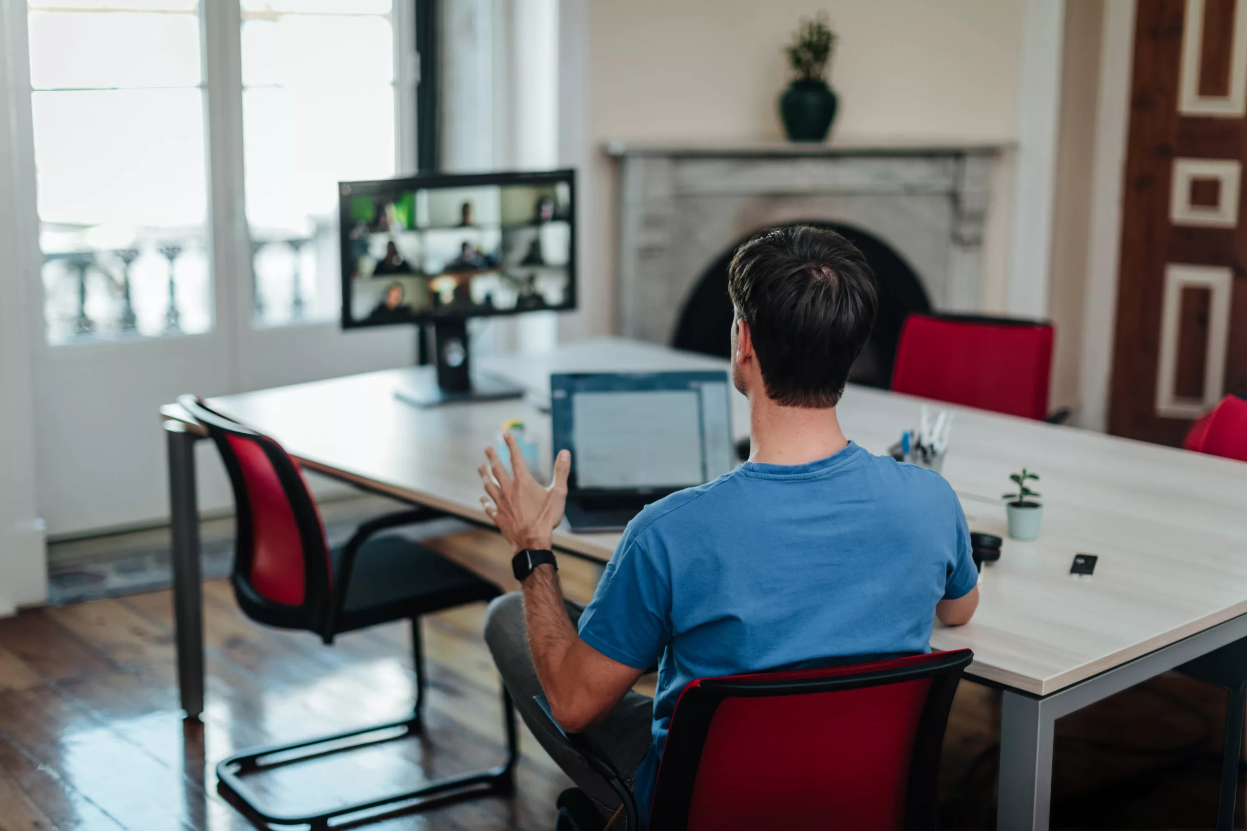 A man in a blue shirt on a video call in a modern office setting.
